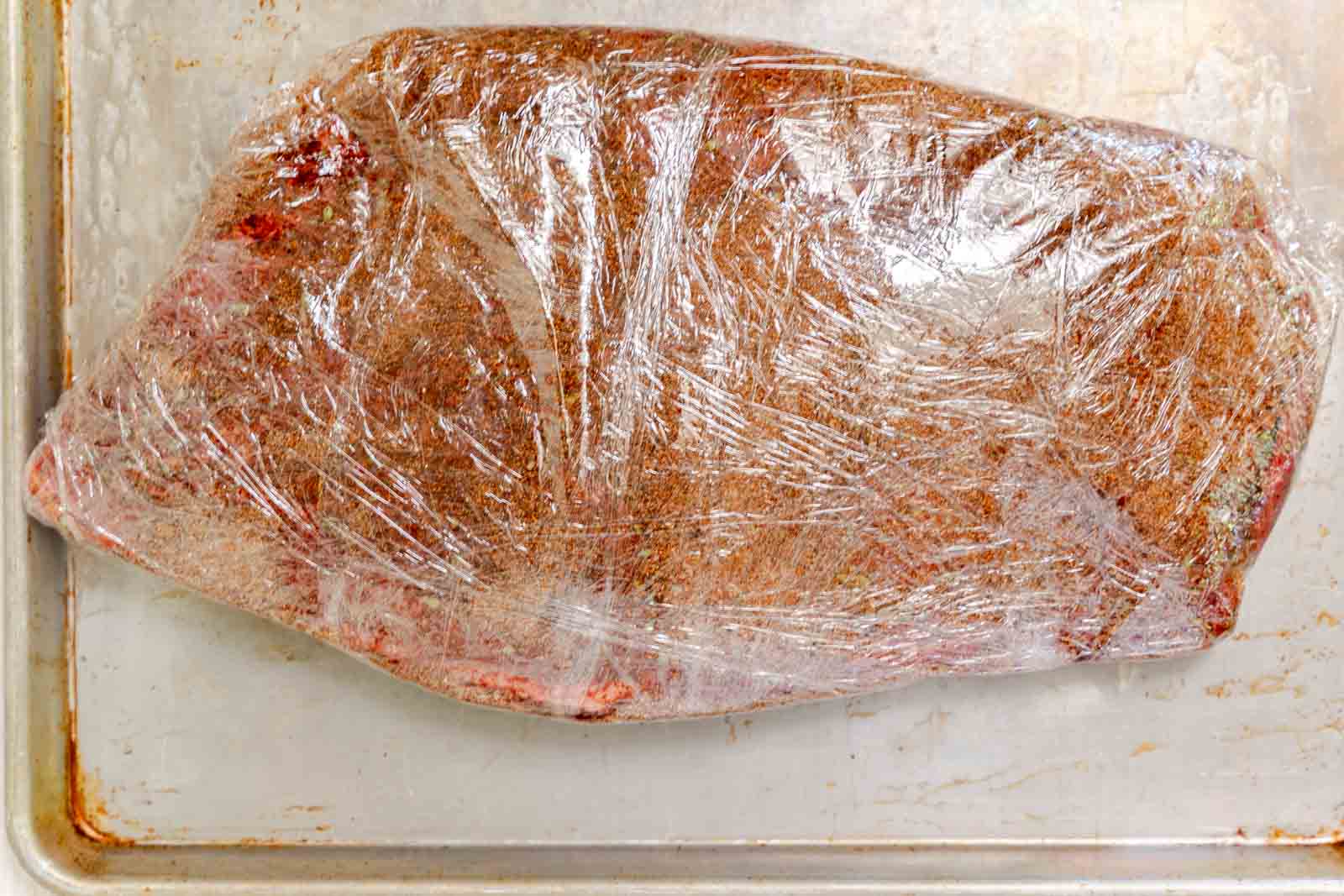 A tightly wrapped beef brisket in plastic wrap sitting on a baking sheet.
