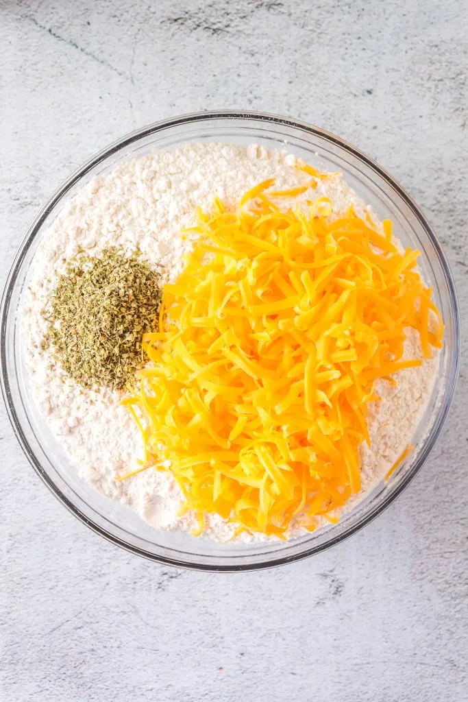 Top down view of a large bowl filled with flour, shredded cheese and Italian seasoning.