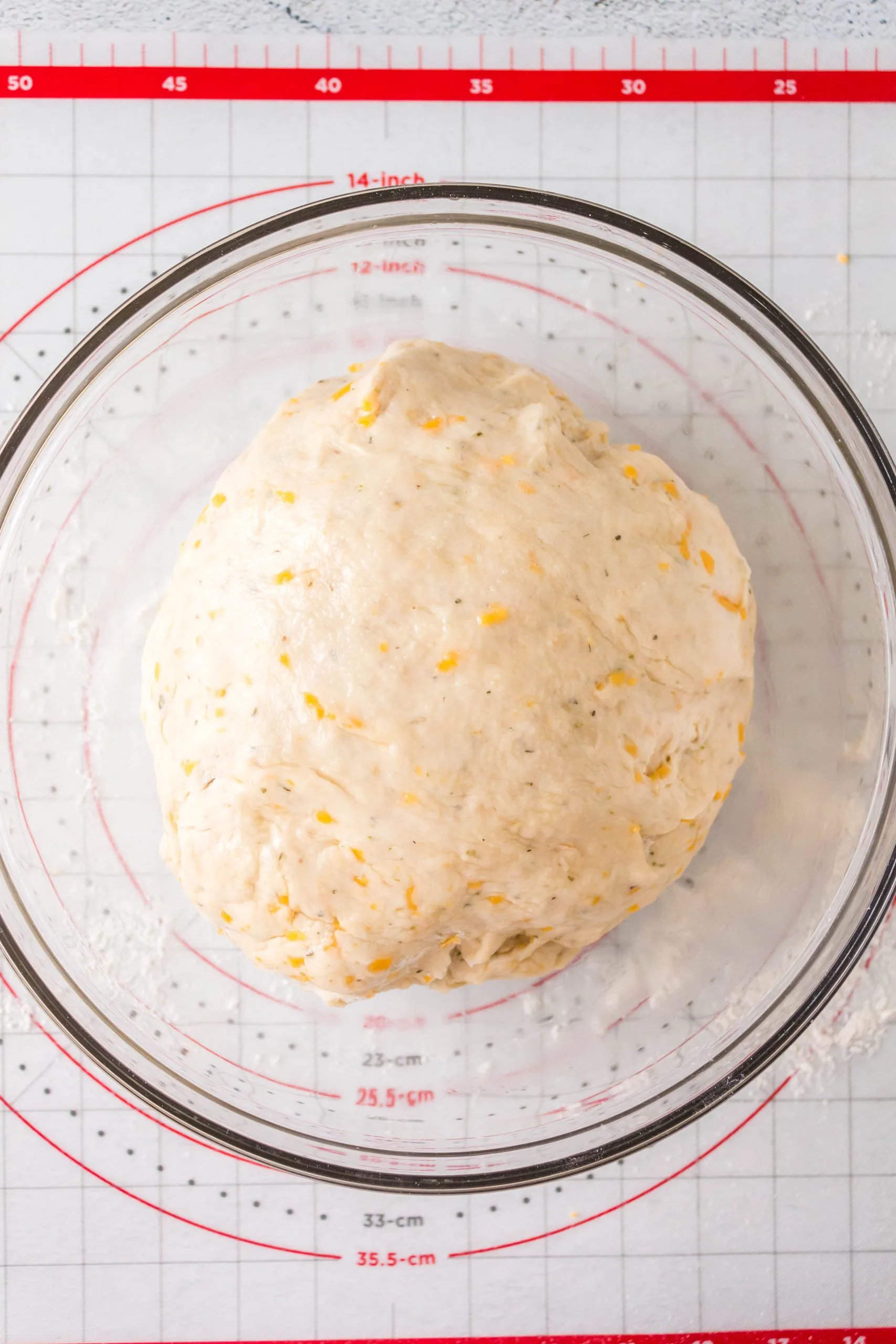 Dough dotted with cheese in a bowl to rise.