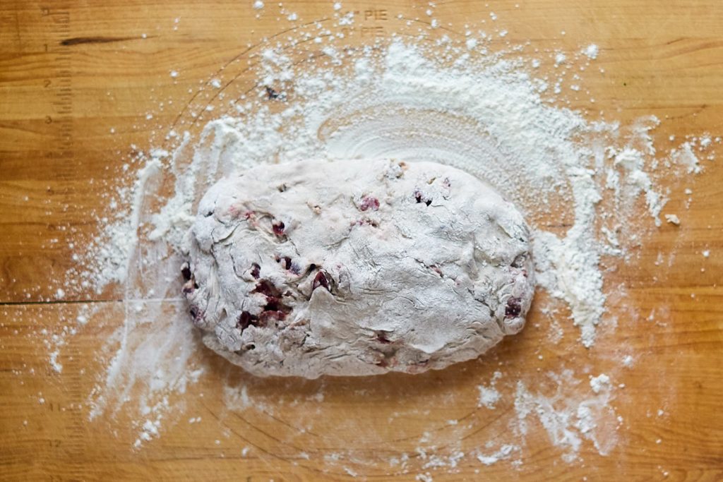 A loaf of shaped cranberry bread covered with flour before it's baked.