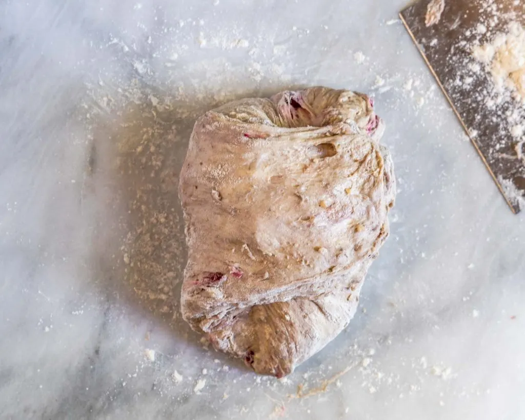 Image showing the left side of dough stretched to the right in order to shape a loaf of sourdough.