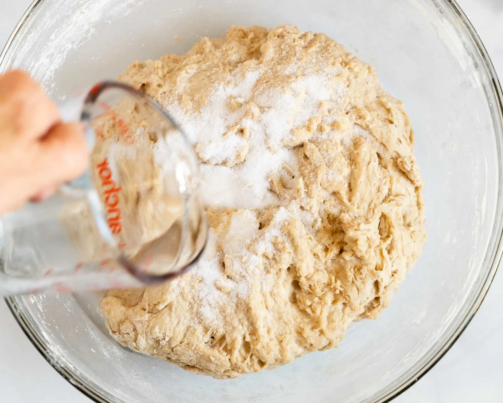 Salt and water added to bread dough in a bowl.
