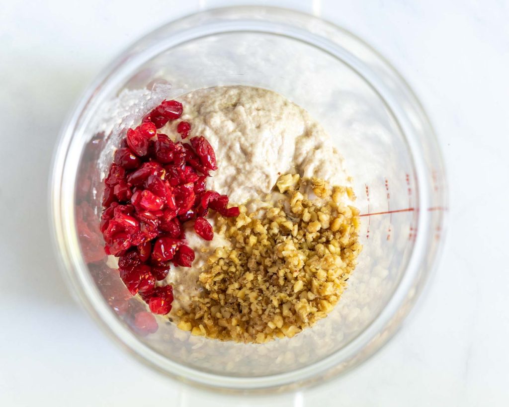 A proofing bucket filled with bread dough, chopped cranberries and walnuts.