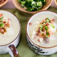 Top down view of two bowls of potato soup topped with onions bacon and cheese.