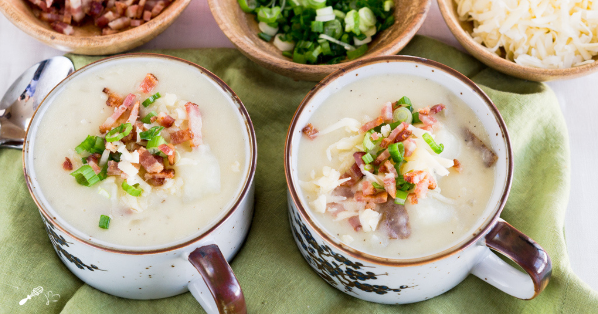 Top down view of two bowls of potato soup topped with onions bacon and cheese.