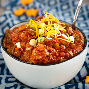 Tableview of a bowl of pork chili topped with onion and cheese.