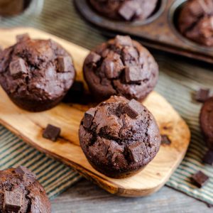 A chocolate pumpkin muffin sitting on a cutting board garnished with chunks of chocolate.