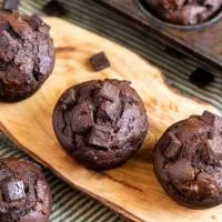 Several chocolate muffins with pumpkin sitting on a cutting board and topped with chunks of chocolate