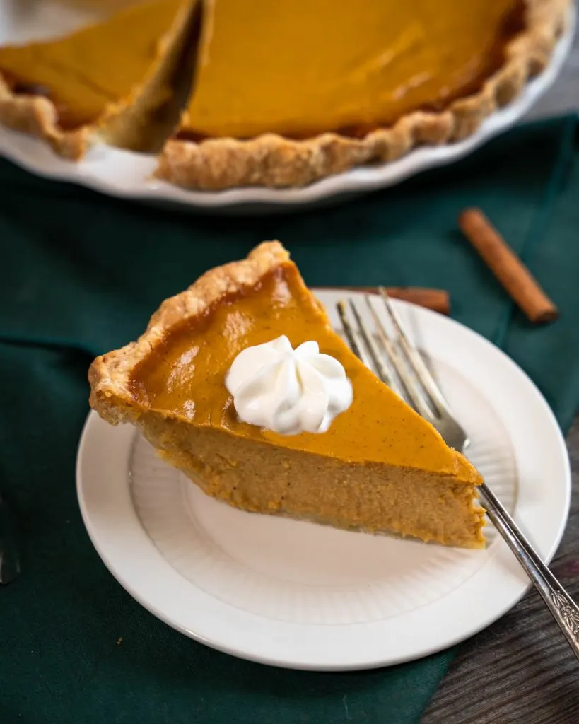 3/4 view of a slice of pumpkin pie from scratch topped with whipped cream.