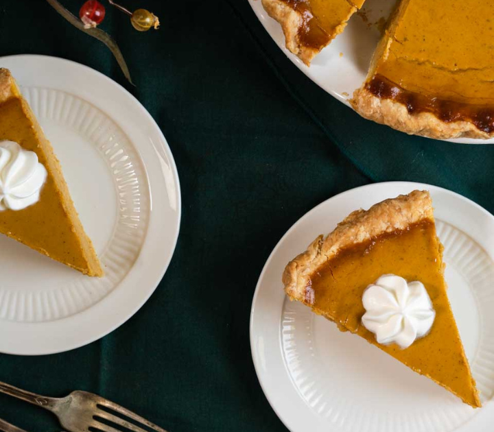 Top down view of two slices of pumpkin pie topped with a swirl of whipped cream.
