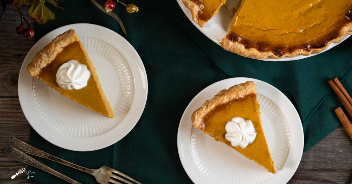 Top down view of two slices of pumpkin pie topped with a swirl of whipped cream.