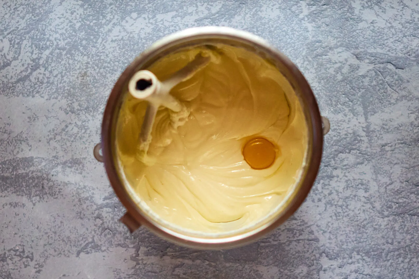 An egg added to a cream cheese batter in a bowl