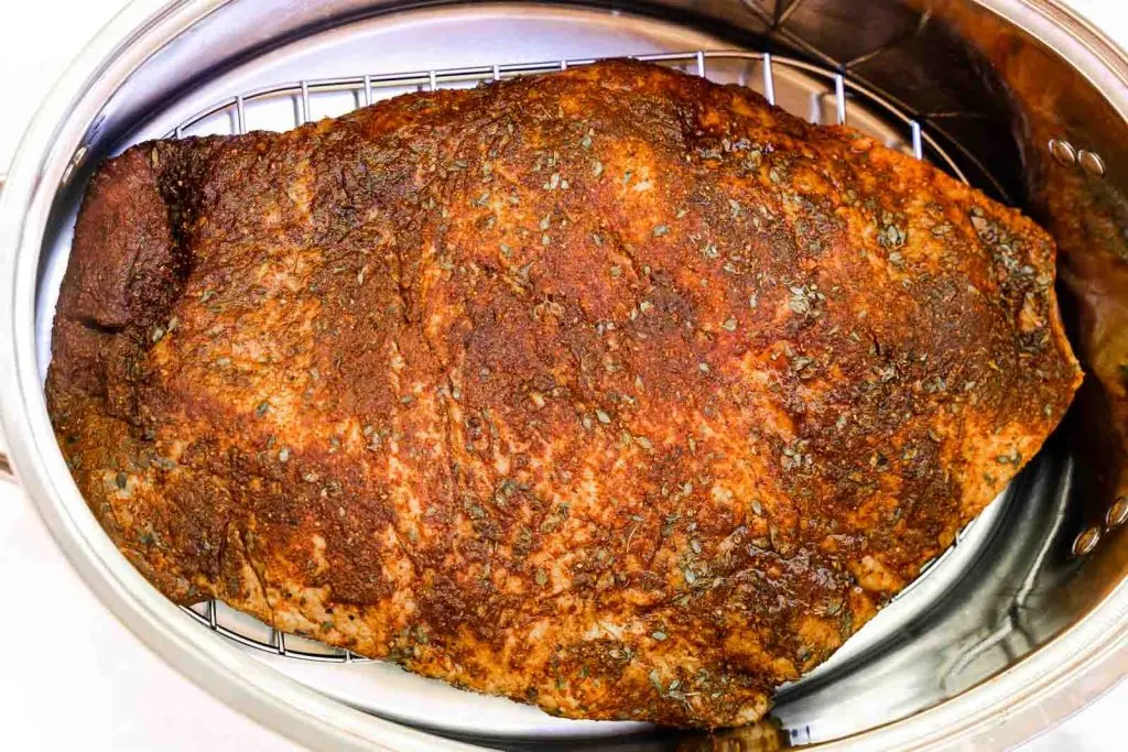 A dry rubbed beef brisket sitting on a grate inside a roasting pan.
