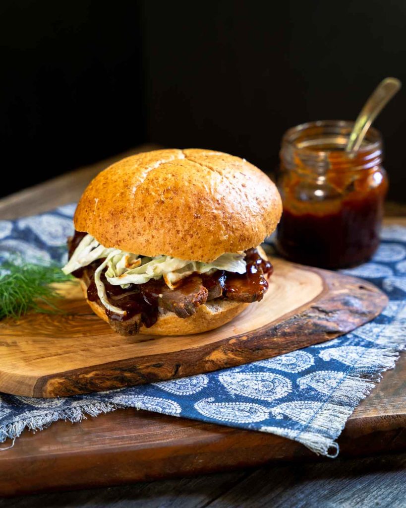 Side shot of a barbecue brisket sandwich topped with cabbage slaw sitting on a cutting board.