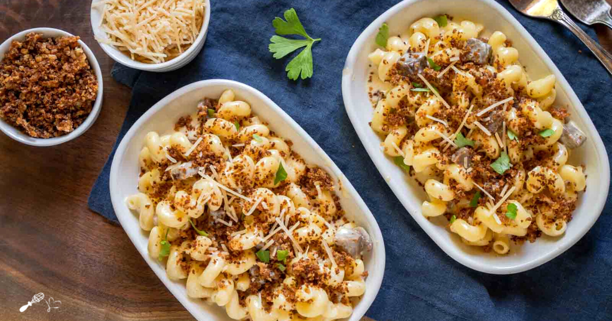 Top down view of two dishes of cavatappi mac and cheese with chunks of brisket topped with Browned Panko Breadcrumbs.