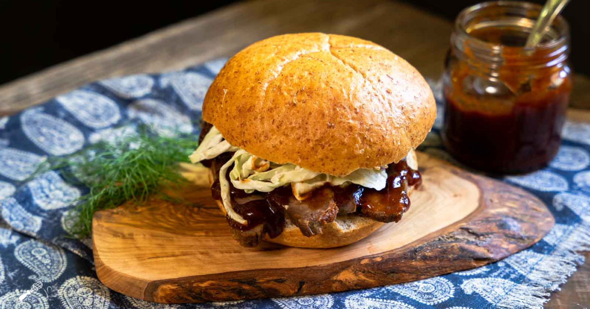 Side view of a sandwich topped with sliced beef, bbq sauce and cabbage coleslaw