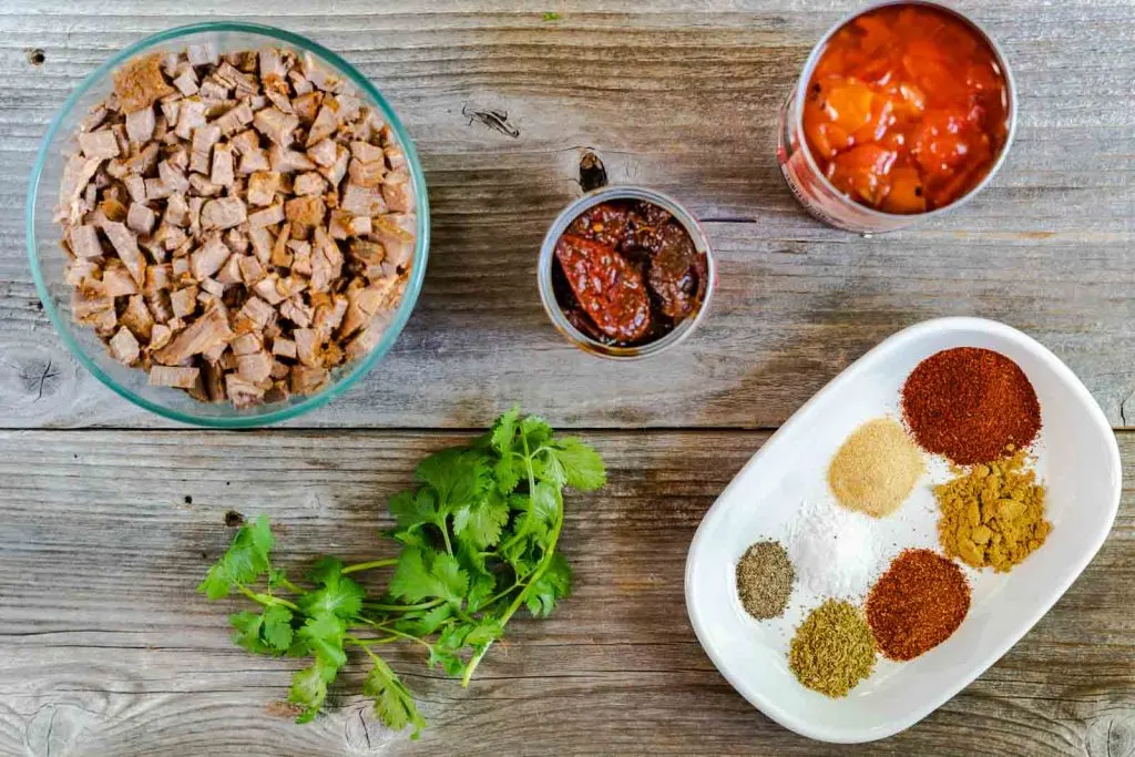 Ingredients to make brisket tacos including beef, cilantro, chili in adobe sauce, and spices.