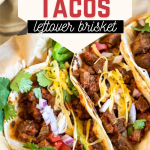 Tope down view of three beef brisket tacos garnished with cilantro, cheese, tomatoes and onion in a basket.