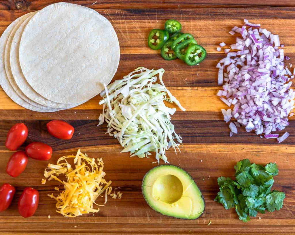 Top down view of garnishes for beef brisket tacos including tomatoes, cheese, onion, cabbage, avocado and cilantro.