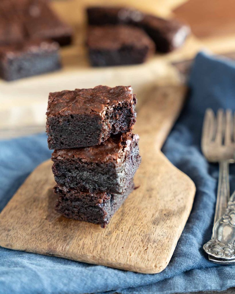 Three dark chocolate brownies with cocoa powder with a bite taken out of the top one.