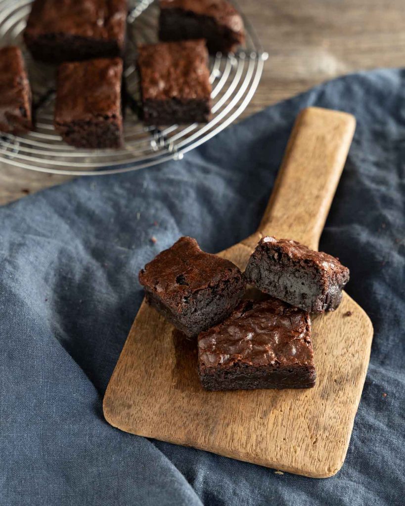 Three pieces of Dark Chocolate Brownies leaning next to each other on a wooden butter paddle.