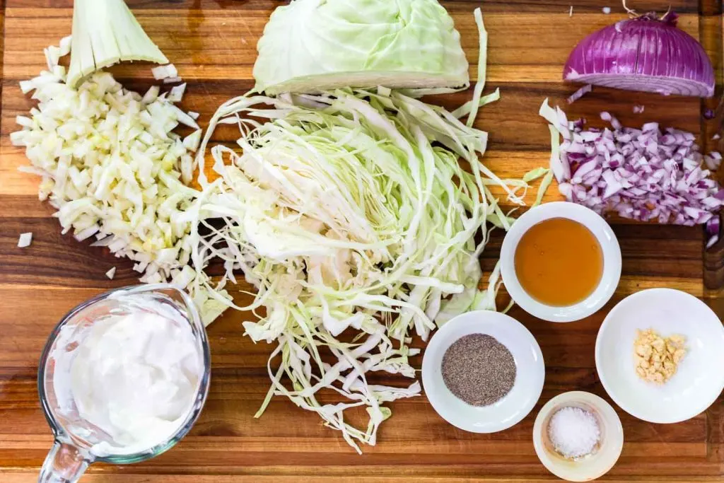 Top down view of the ingredients used to make fennel slaw including fennel, cabbage, onion, sour cream, honey, garlic, salt, and pepper.