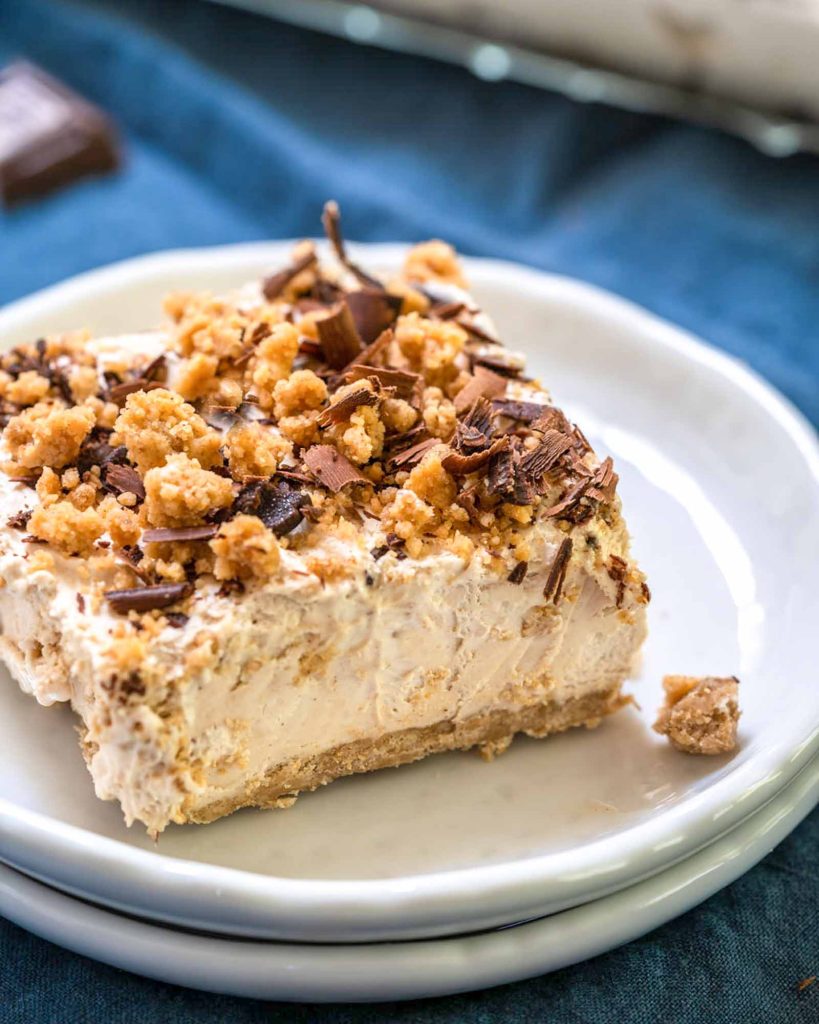 Angled view of a slice of frozen peanut butter and cream cheese dessert topped with peanut butter crumbles and shaved chocolate