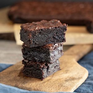 a stack of three chocolate fudge brownies on a wooden butter paddle.
