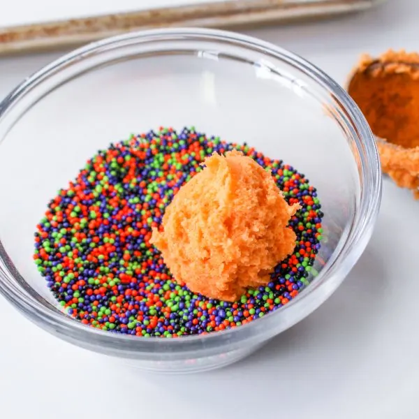 A ball of halloween blossom cookie batter sitting in a bowl of sprinkles