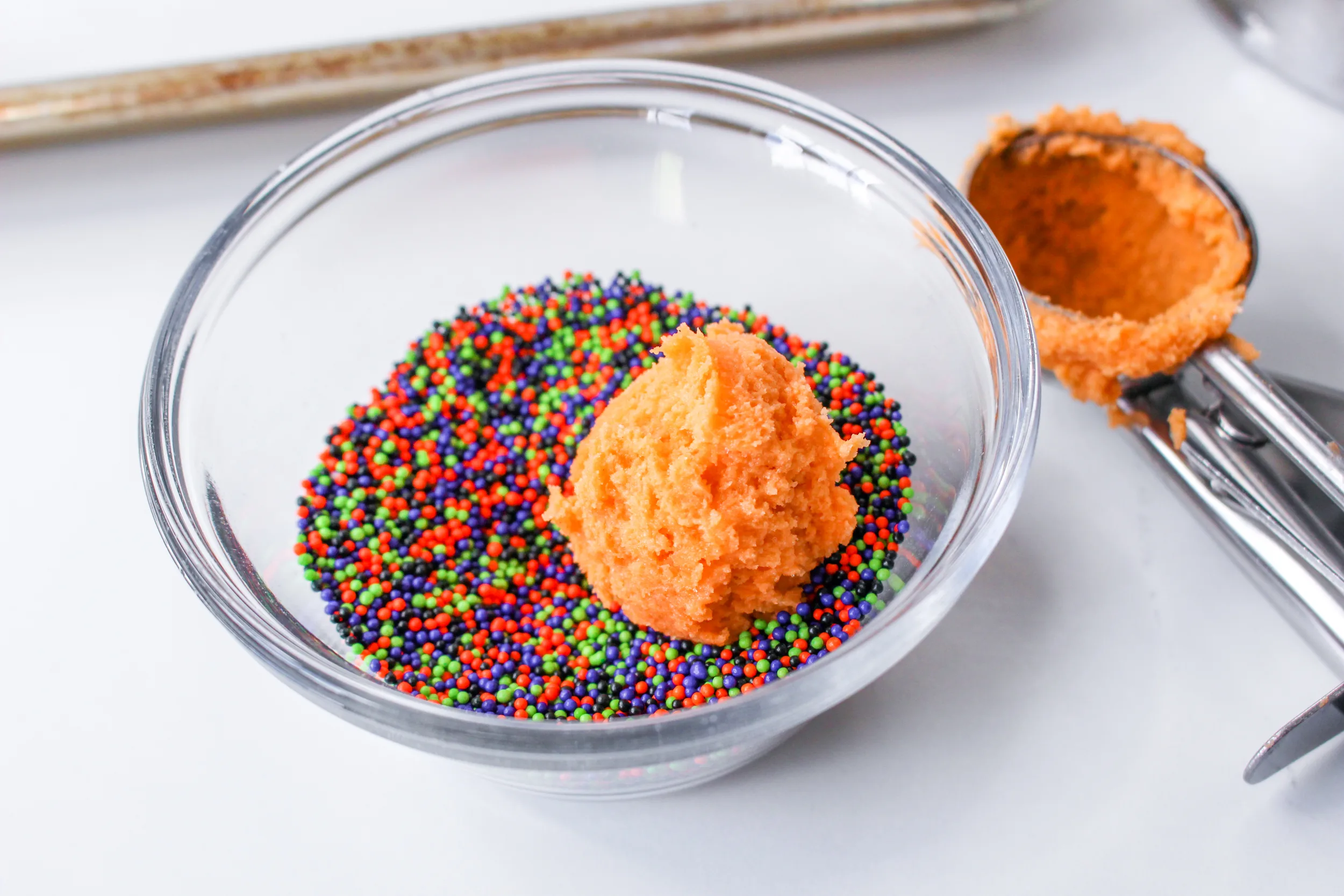 A ball of halloween blossom cookie batter sitting in a bowl of sprinkles