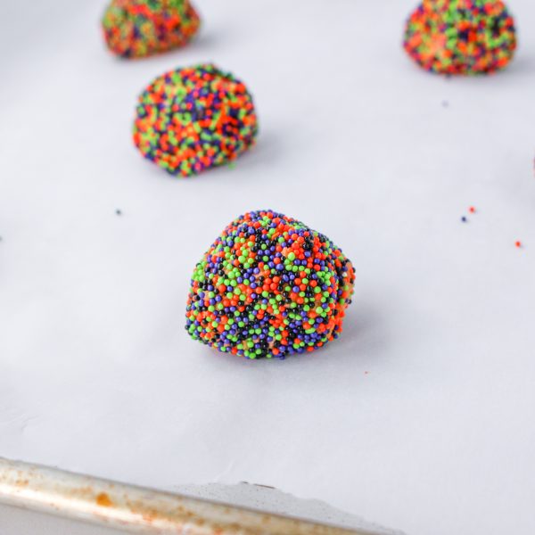 Cookie batter rolled in sprinkles scooped onto parchment paper lined cookie sheet.