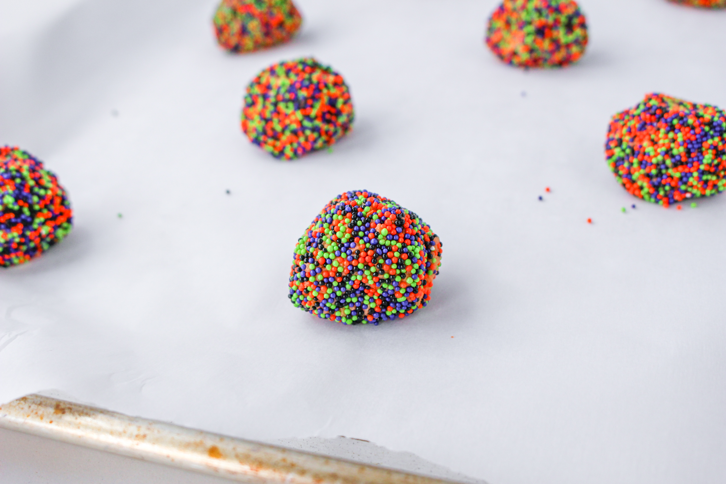 Cookie batter rolled in sprinkles scooped onto parchment paper lined cookie sheet.