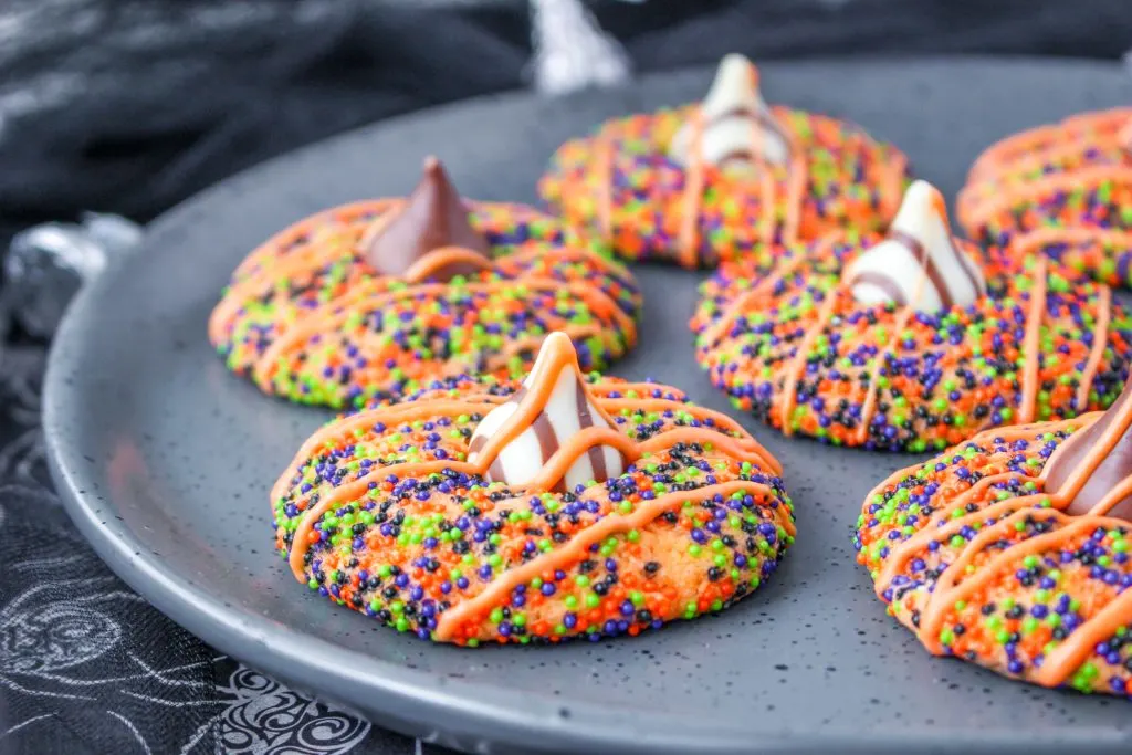Colorfully sprinkled blossom cookies with candy kisses in the center and an orange glaze stripped across them for a Halloween Cookie Party