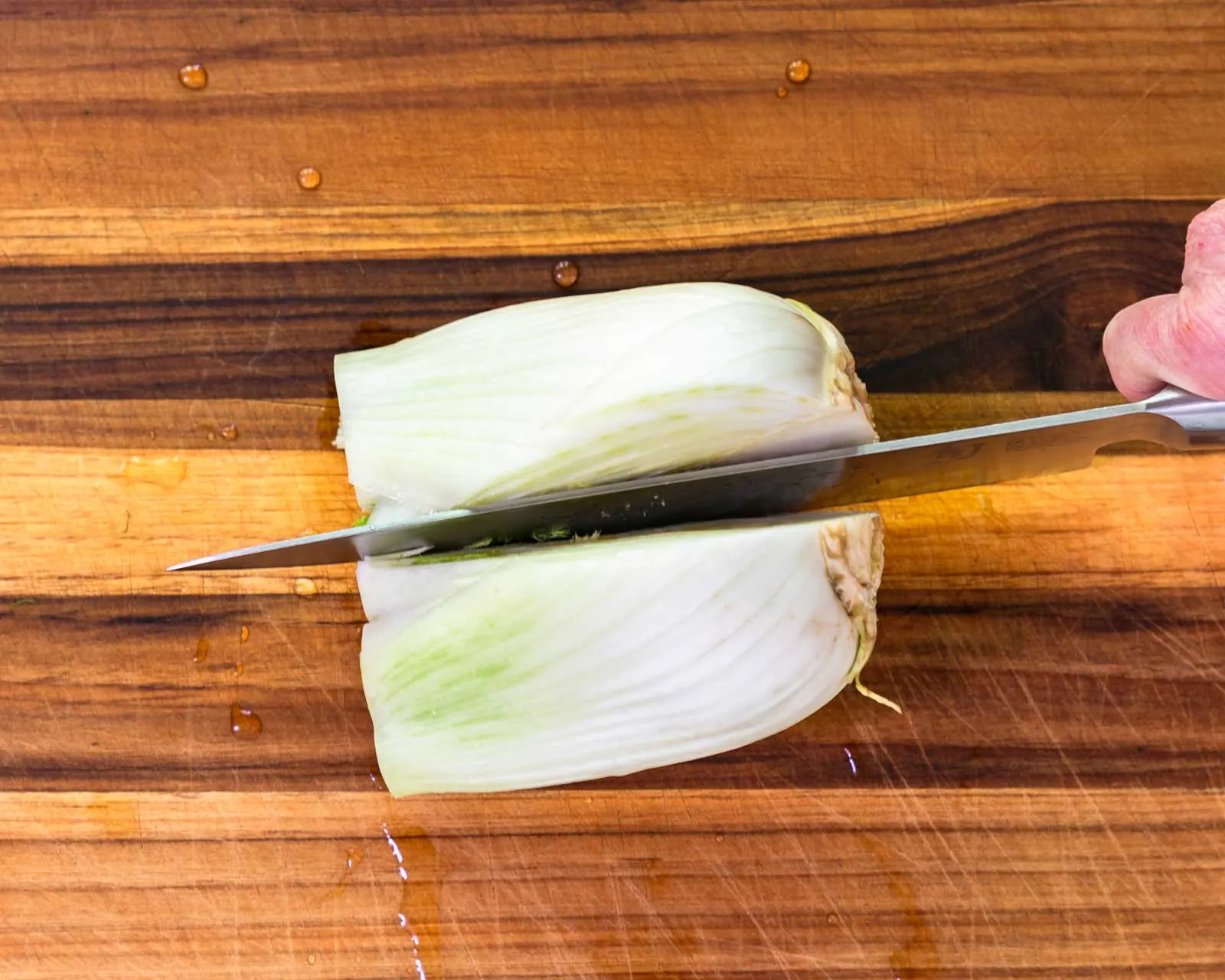 A fennel bulb with the top fronds cut off and being sliced vertically.