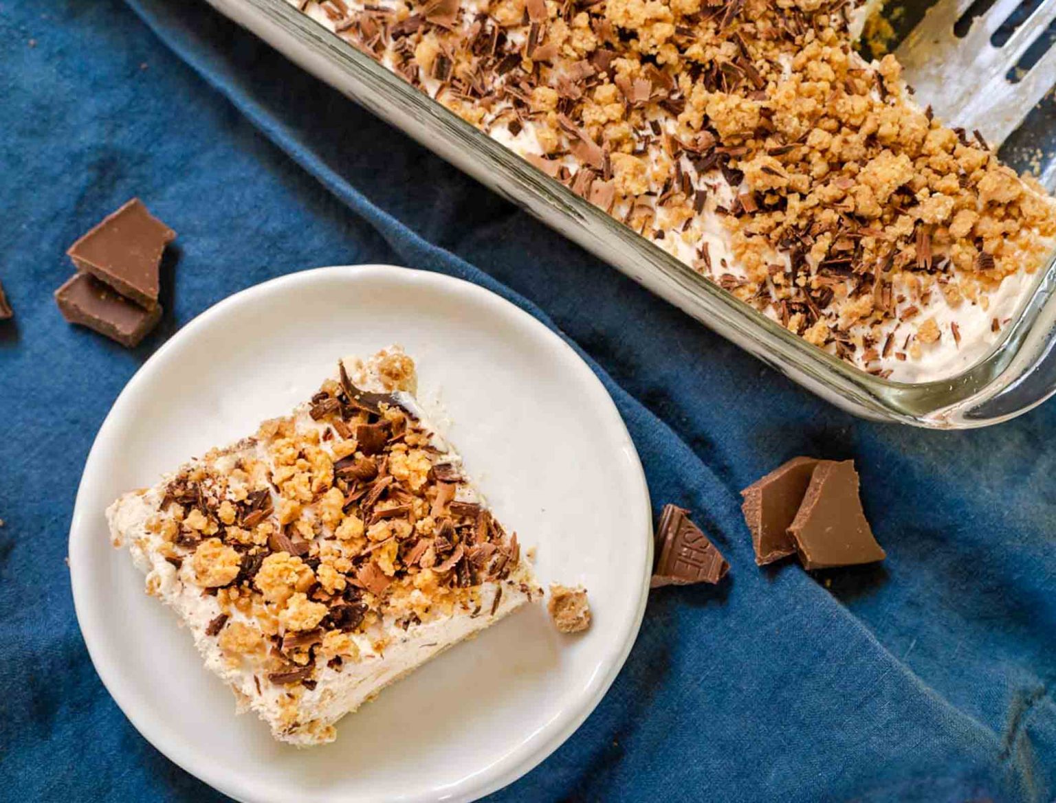 Top down view of a piece of frozen peanutbutter dessert on a plate surrounded by the pan of dessert.