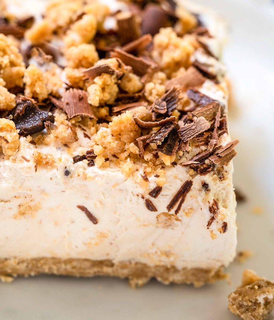 Close up square of frozen cheese cake recipe topped with peanut butter crumble and chocolate shavings.