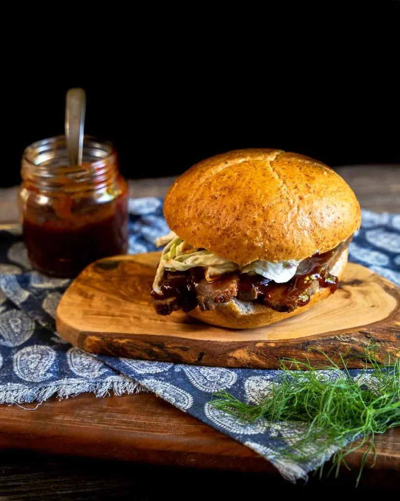 A sideview of a bbq brisket sandwich topped with slaw and slathered in bbq sauce.