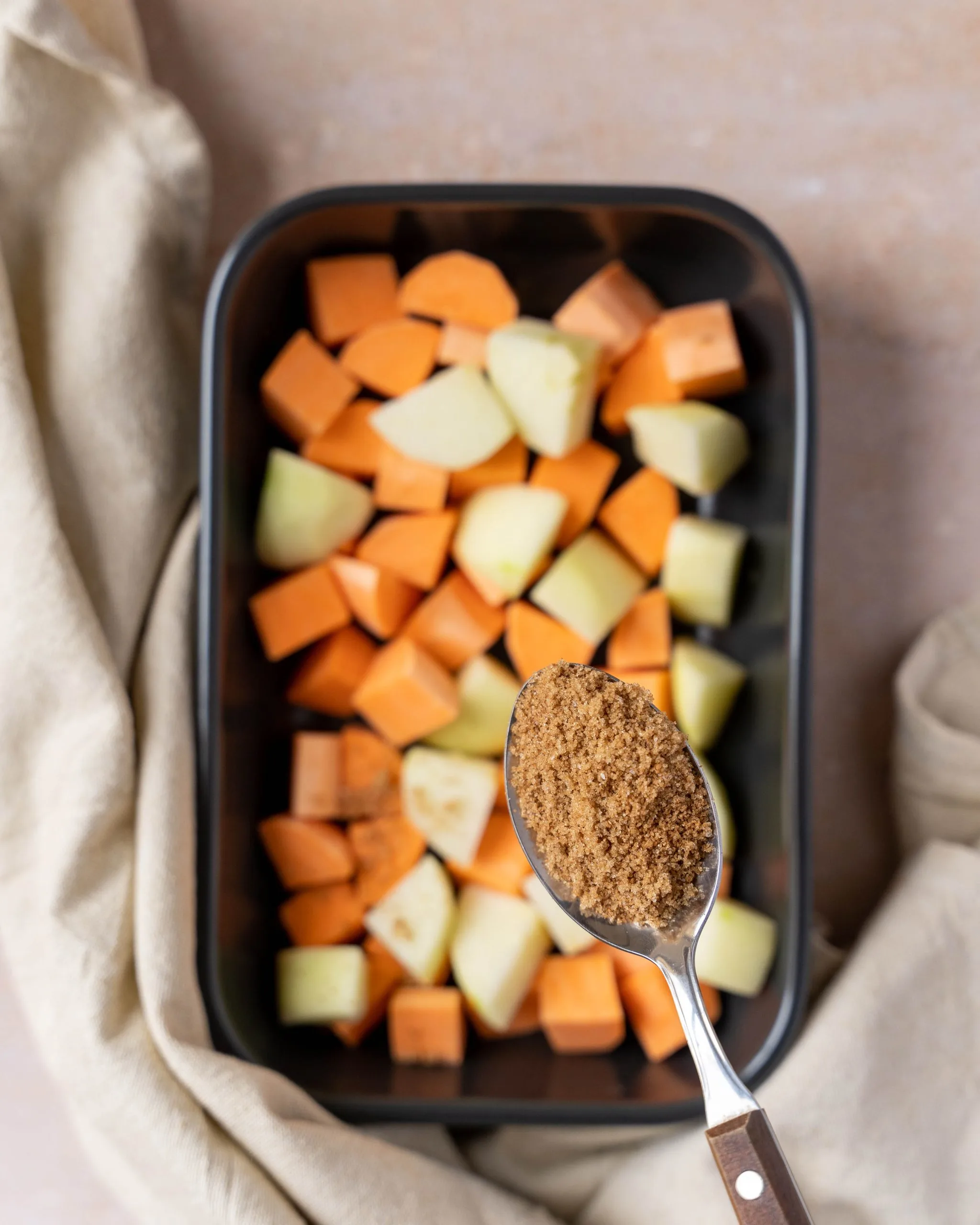 A spoon of brown sugar topping hovering over diced apples and sweet potatoes