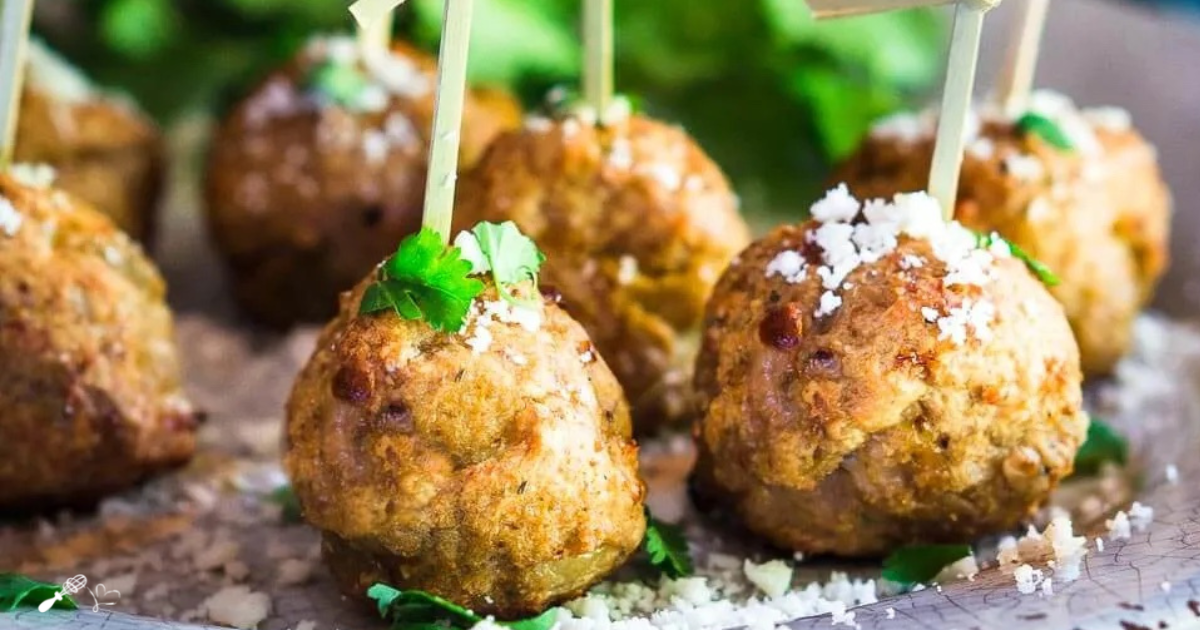 Side view of green chile meatballs skewered with bamboo picks and garnished with cotija and cilantro.