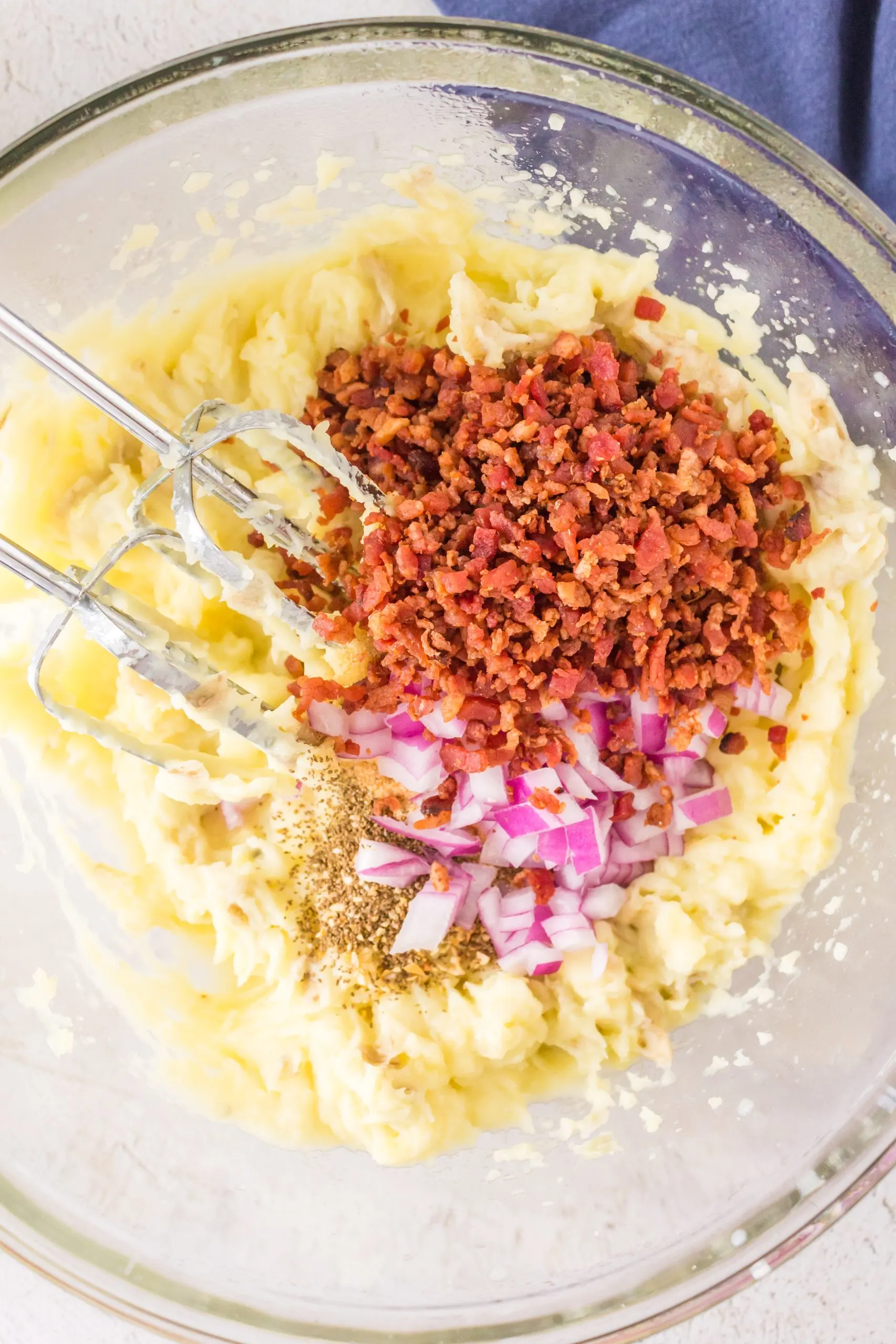 Chopped bacon, onion, and pepper added to a bowl of mashed potatoes