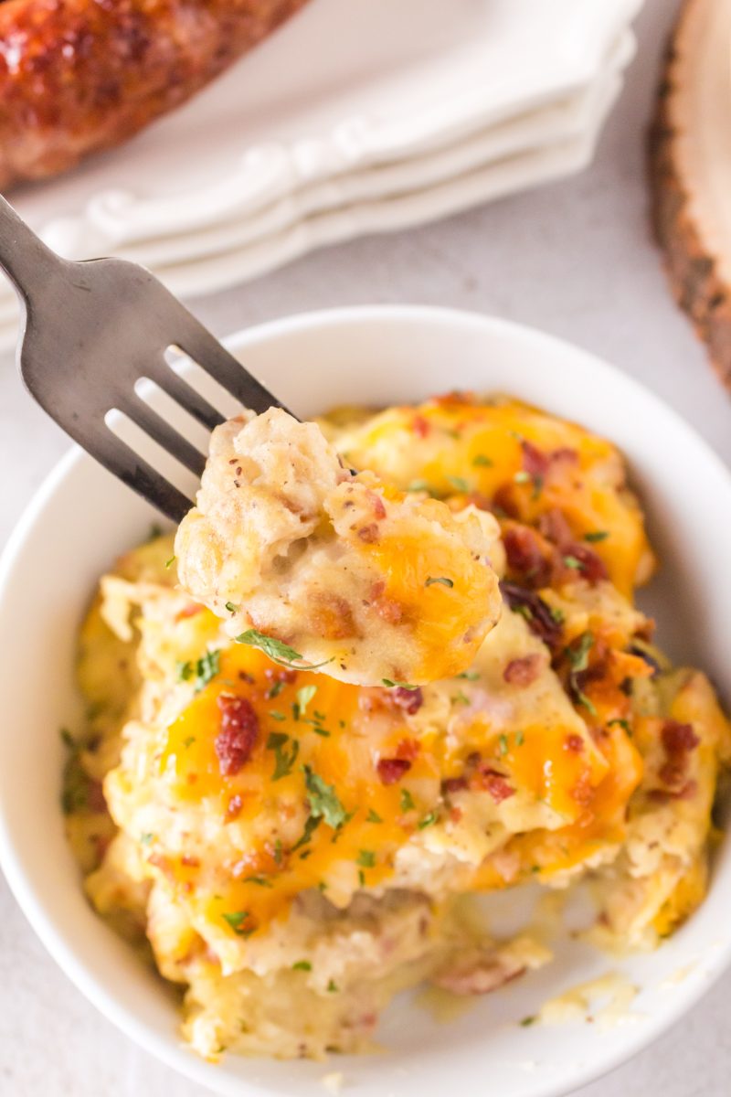 A fork full of cheesy potato casserole topped with cheese and bacon.