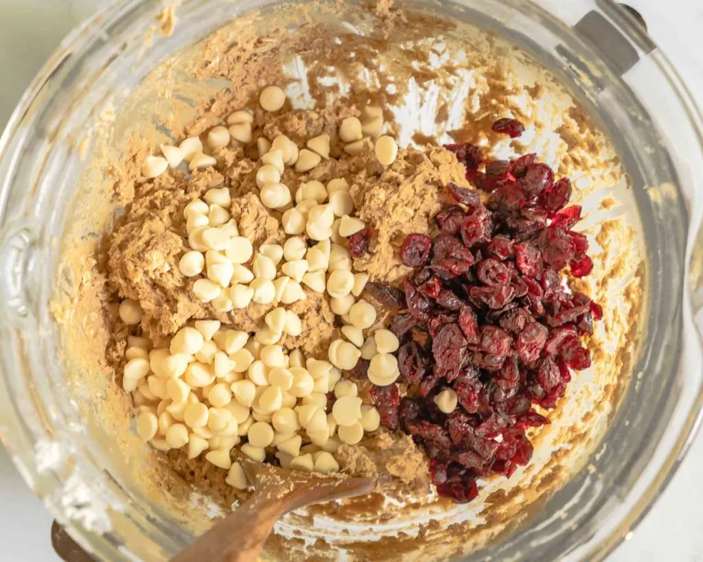 Top down view of mixing bowl filled with cookie dough, white chocolate chips and dried cranberries - very colorful!