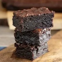 a stack of three chocolate fudge brownies on a wooden butter paddle.