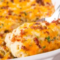 A spoon dipping into a potatoe casserole lifting melted cheese and bacon topping.