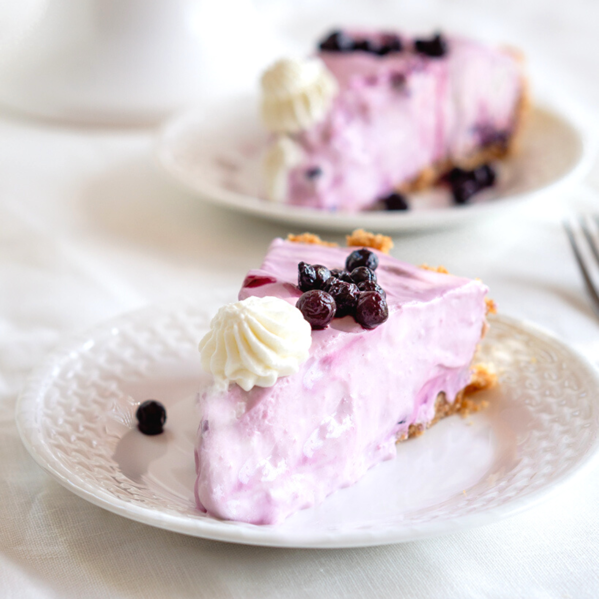 Forward table view of a slice of blue berry cream cheese lemonade pie with a piped star of whipped topping and wild blueberries on top.