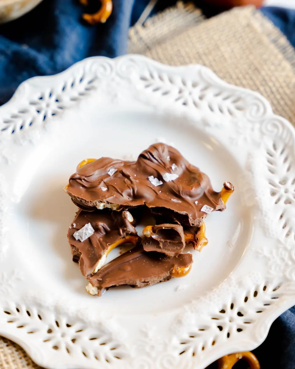 Pieces of a chocolate bark with pretzels sitting on a white plate - hostess at heart