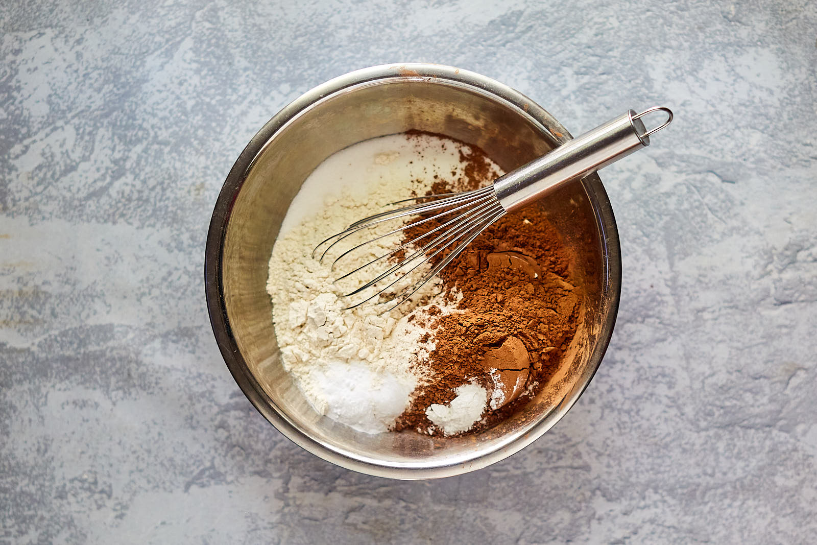 Dry ingredients added to a metal bowl with a whisk.