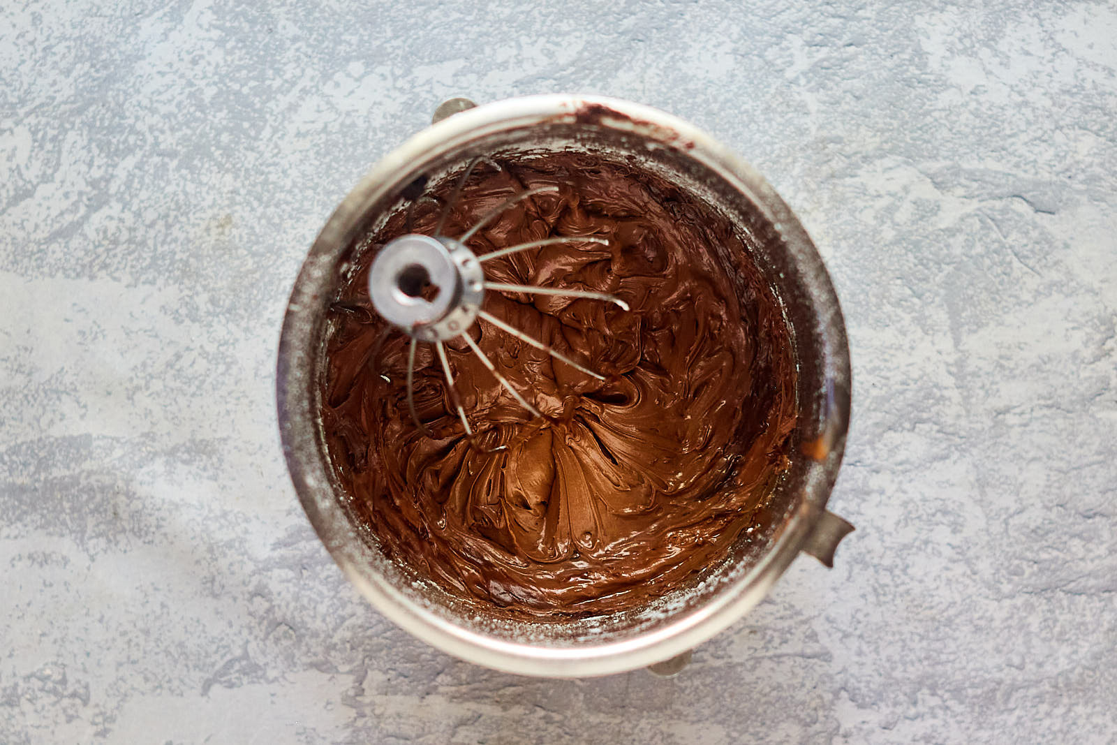 Top down view of thick chocolate buttercream frosting in a mixing bowl