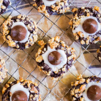 Chocolate Thumb Print Blossom Cookies rolled in nuts and sitting on a cooling rack.