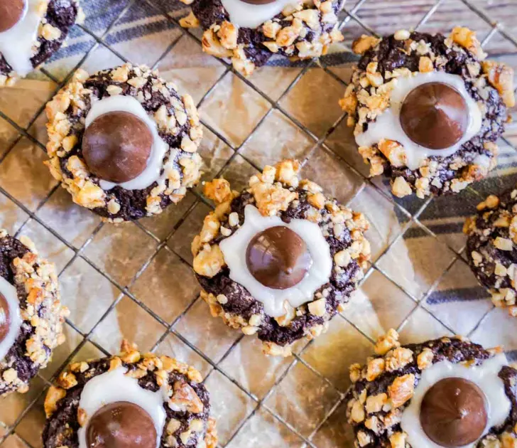 Chocolate Thumb Print Blossom Cookies rolled in nuts and sitting on a cooling rack.